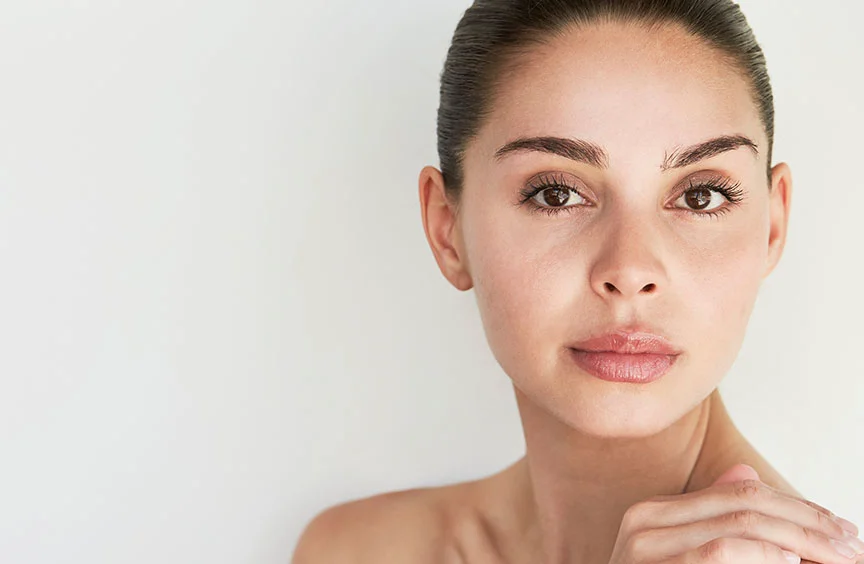 A close-up shot of a woman with a slicked-back bun, resting one hand on her shoulder. Her shoulders are bare, highlighting her elegant and minimalist look. - Liquid Facelift Recovery in Bryn Mawr, PA